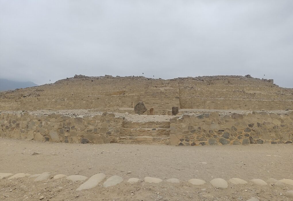 Pirámide escalonada de piedra en Caral, con una escalera central y un cielo nublado