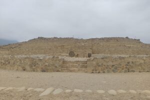Pirámide escalonada de piedra en Caral, con una escalera central y un cielo nublado