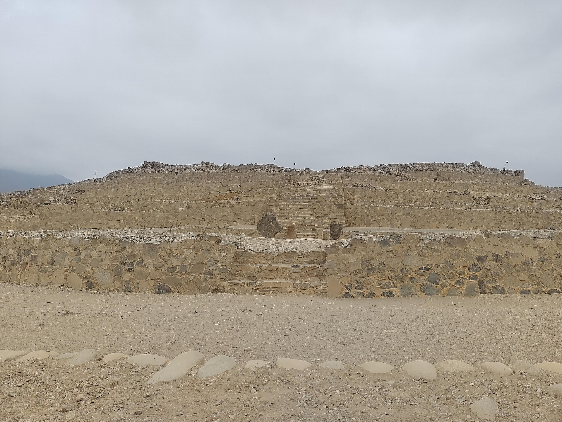 Pirámide escalonada de piedra en Caral, con una escalera central y un cielo nublado