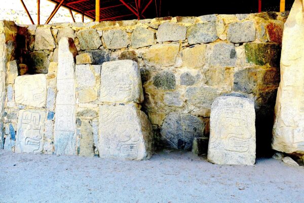 Casma: monolitos de Cerro Sechín con rostros y figuras talladas, frente a un muro de piedras bajo un techo protector