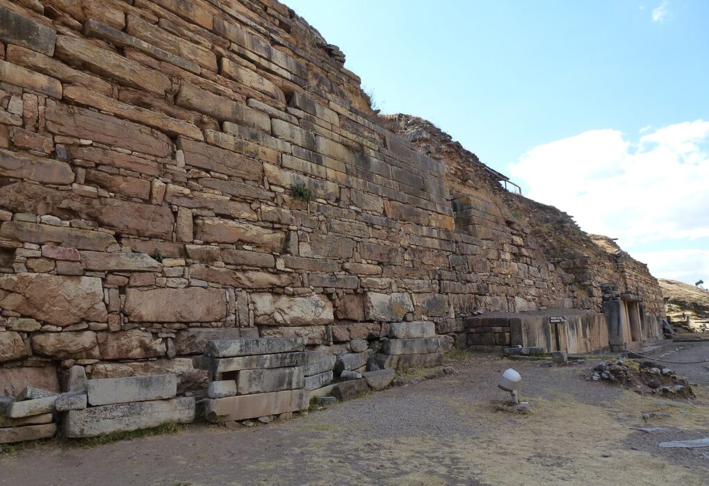 Chavín de Huántar: alto muro de piedras rectangulares del templo, sobre un terreno de tierra y pasto seco, bajo un cielo azul con nubes blancas