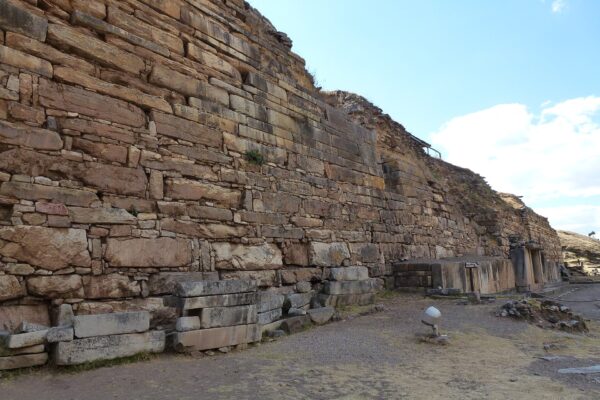 Chavín de Huántar: alto muro de piedras rectangulares del templo, sobre un terreno de tierra y pasto seco, bajo un cielo azul con nubes blancas