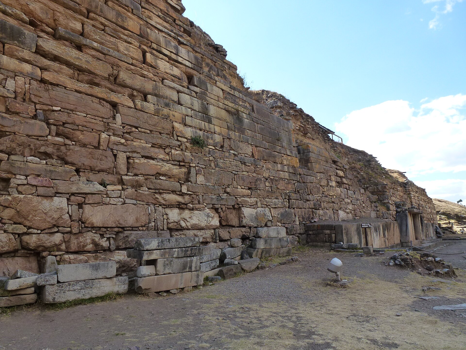 Chavín de Huántar: alto muro de piedras rectangulares del templo, sobre un terreno de tierra y pasto seco, bajo un cielo azul con nubes blancas
