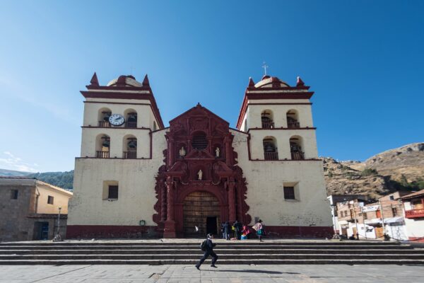 Catedral de Huancavelica, de fachada blanca con portada barroca rojiza y dos torres con campanas, frente a una escalinata, bajo un cielo azul