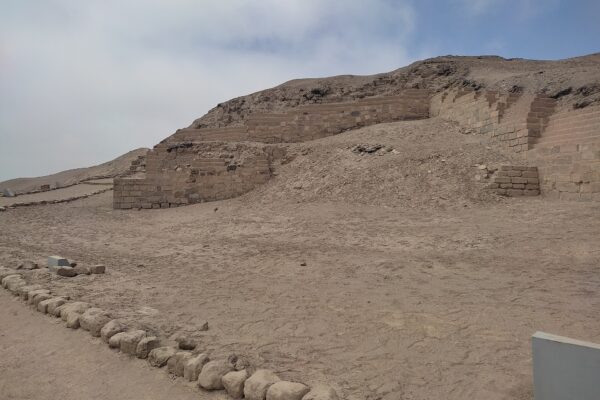 Pachacamac: restos del Templo del Sol, muros de adobe escalonados sobre una loma de tierra, con explanada y piedras alineadas bajo cielo nublado