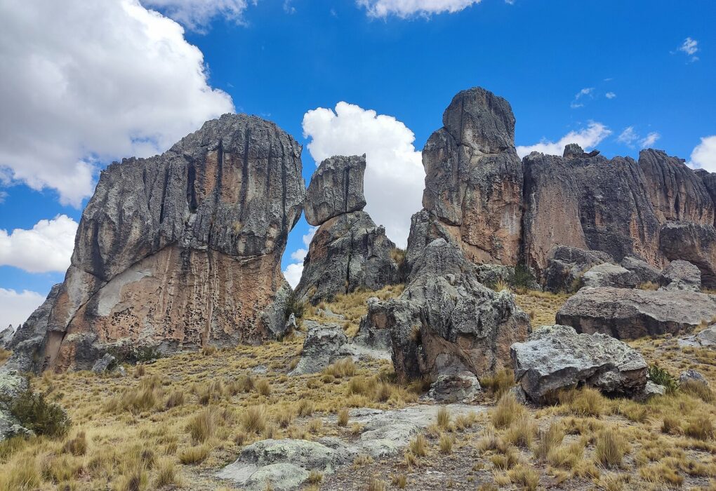 Santuario Nacional de Huayllay: grandes formaciones de roca gris con vetas rojizas sobre una ladera de ichu dorado, bajo un cielo azul con nubes blancas