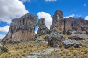 Santuario Nacional de Huayllay: grandes formaciones de roca gris con vetas rojizas sobre una ladera de ichu dorado, bajo un cielo azul con nubes blancas
