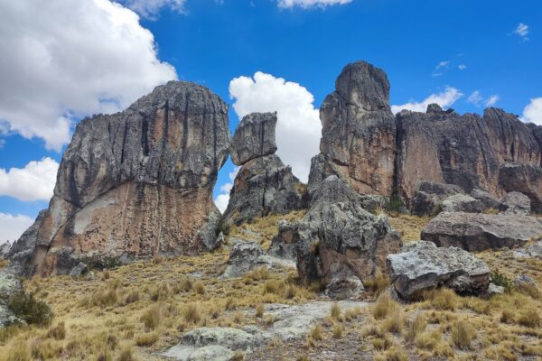 Santuario Nacional de Huayllay: grandes formaciones de roca gris con vetas rojizas sobre una ladera de ichu dorado, bajo un cielo azul con nubes blancas