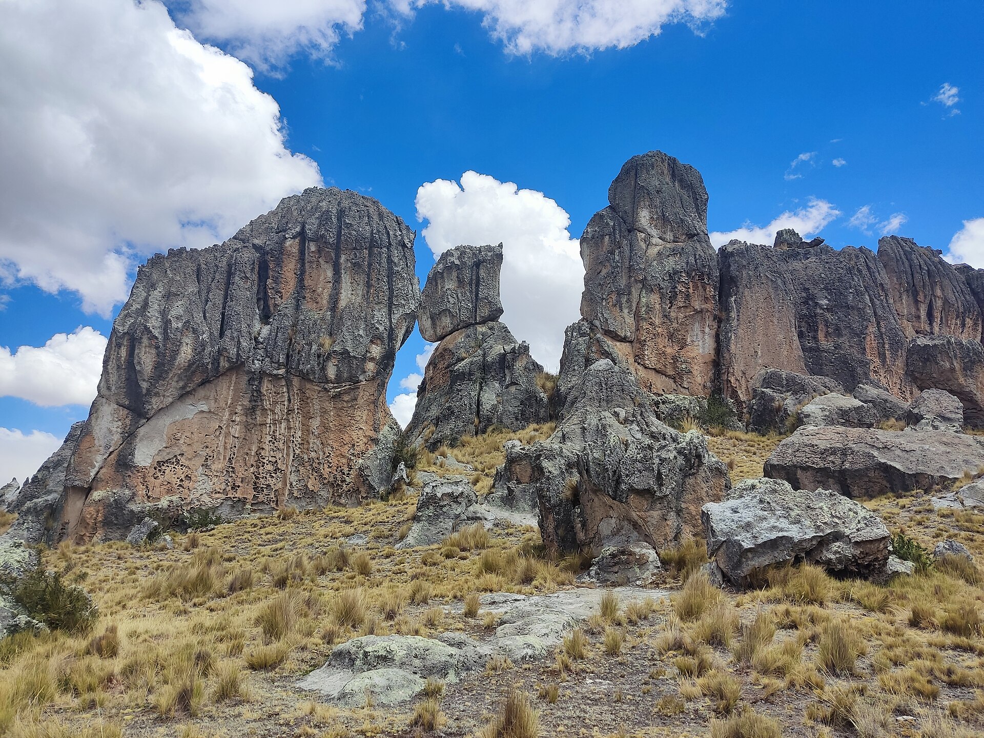 Santuario Nacional de Huayllay: grandes formaciones de roca gris con vetas rojizas sobre una ladera de ichu dorado, bajo un cielo azul con nubes blancas
